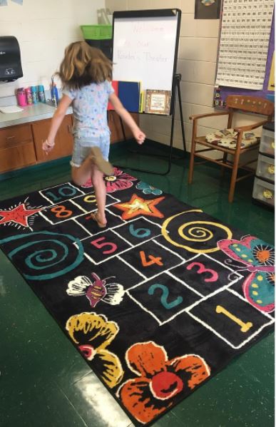 Second grader plays hopscotch on Mohawk Home's interactive classroom area rug