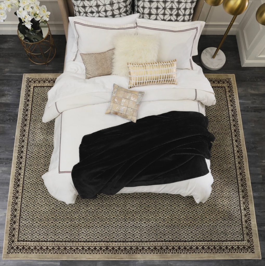 Overhead view of full size bed, nightstand and lamp, with area rug placed under 3/4 of the bed.