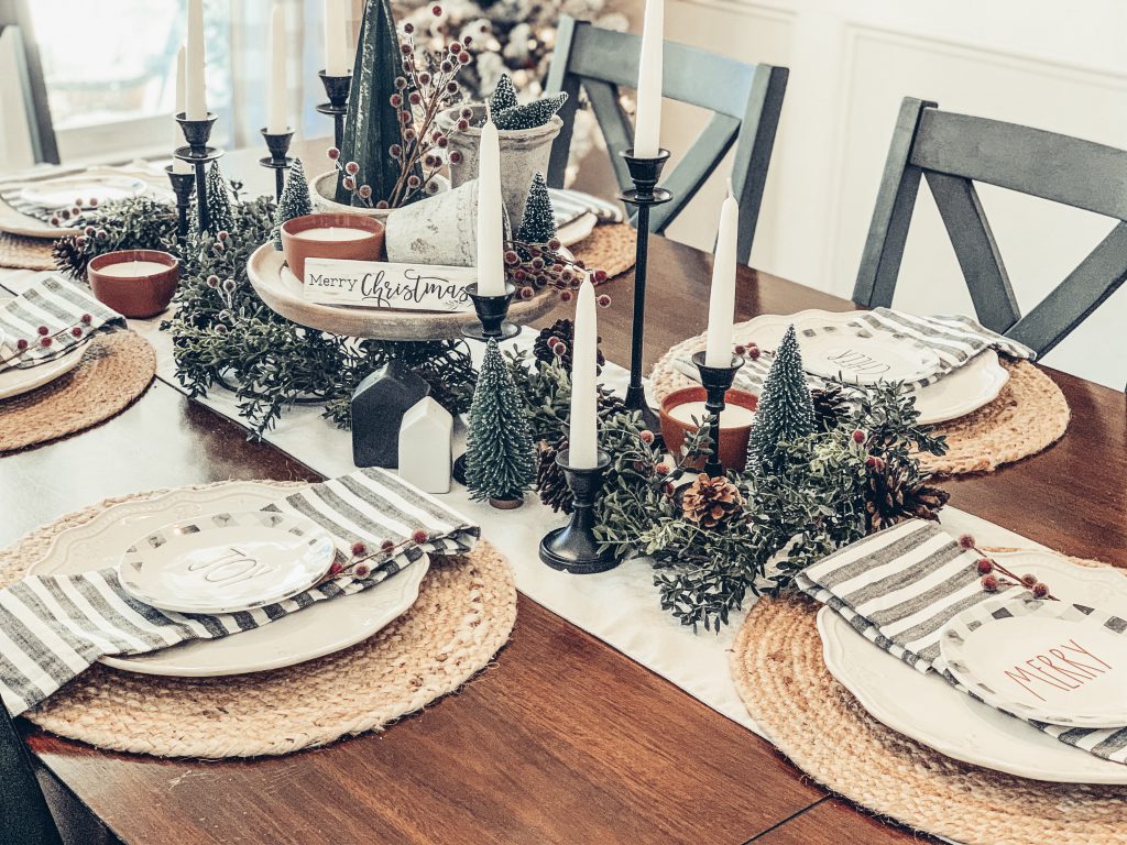 A table decorated for Christmas with bottle brush trees, candles, jute placemats and red berries.
